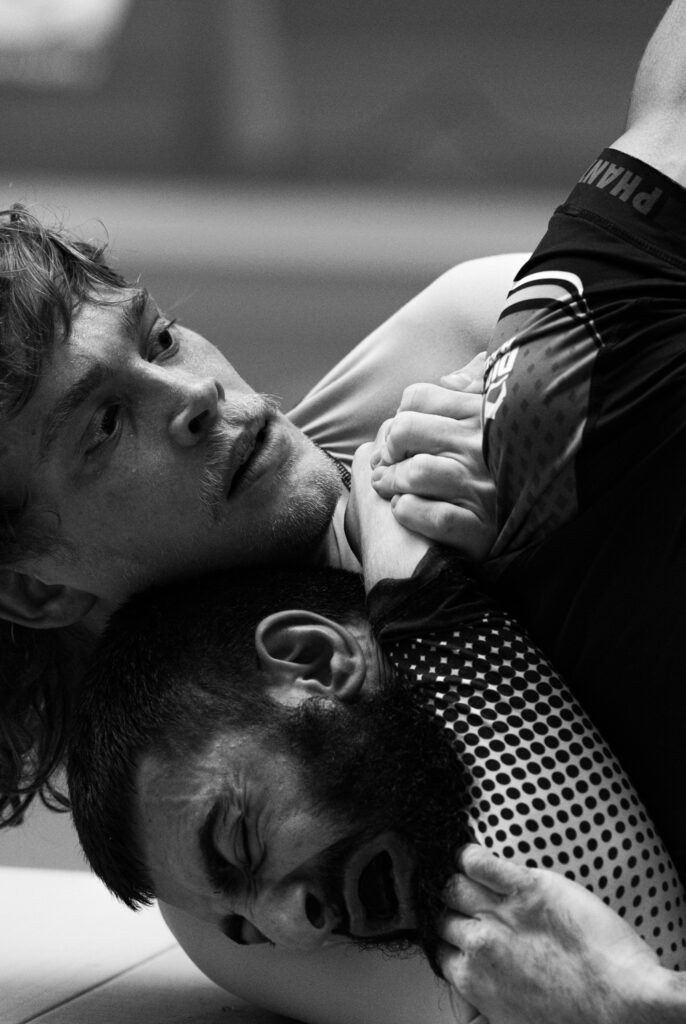 Die Aufnahme zeigt einen Moment intensiven Kampfsports, vermutlich Brazilian Jiu-Jitsu oder Mixed Martial Arts. Die Körperlichkeit und die Konzentration der beteiligten Personen sind deutlich erkennbar.