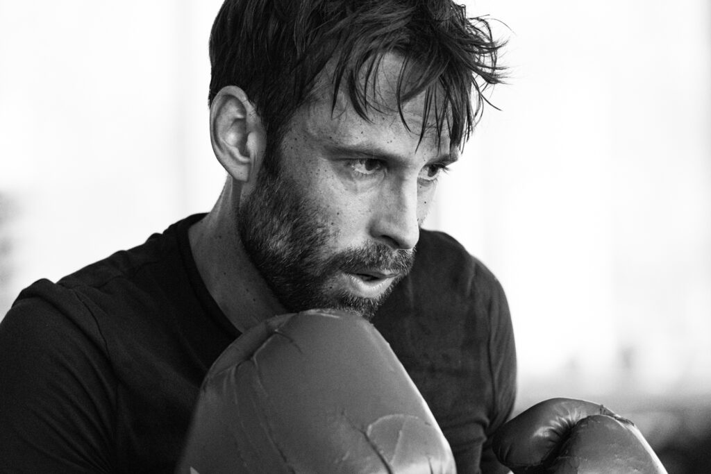 Die Aufnahme zeigt einen Mann, vermutlich ein Boxer, während er sich im Ringside Gym in Berlin, Lichtenberg, Der Fokus liegt auf dem Gesicht des Mannes, der Anstrengung und Konzentration widerspiegelt.