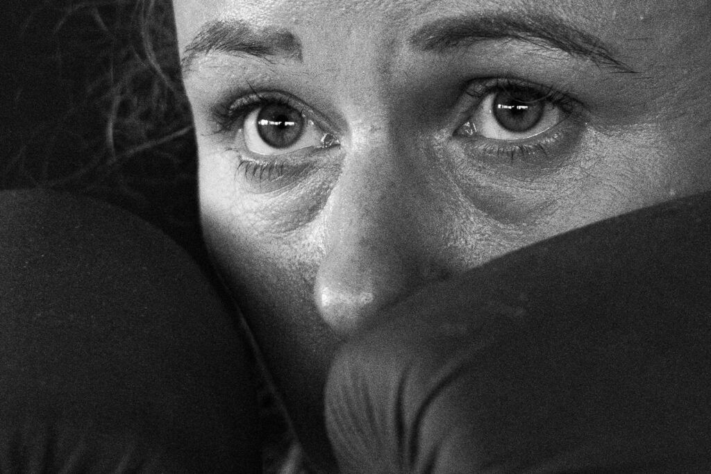 Die Aufnahme zeigt einen Nahbereich einer Person, vermutlich ein Boxer/eine Boxerin, während er/sie Kampfsporttraining im Ringside Gym in Berlin-Lichtenberg durchführt. Die dunkle Hintergrund und der Fokus auf das Gesicht erzeugen eine intensive Atmosphäre des Trainings und der Konzentration.