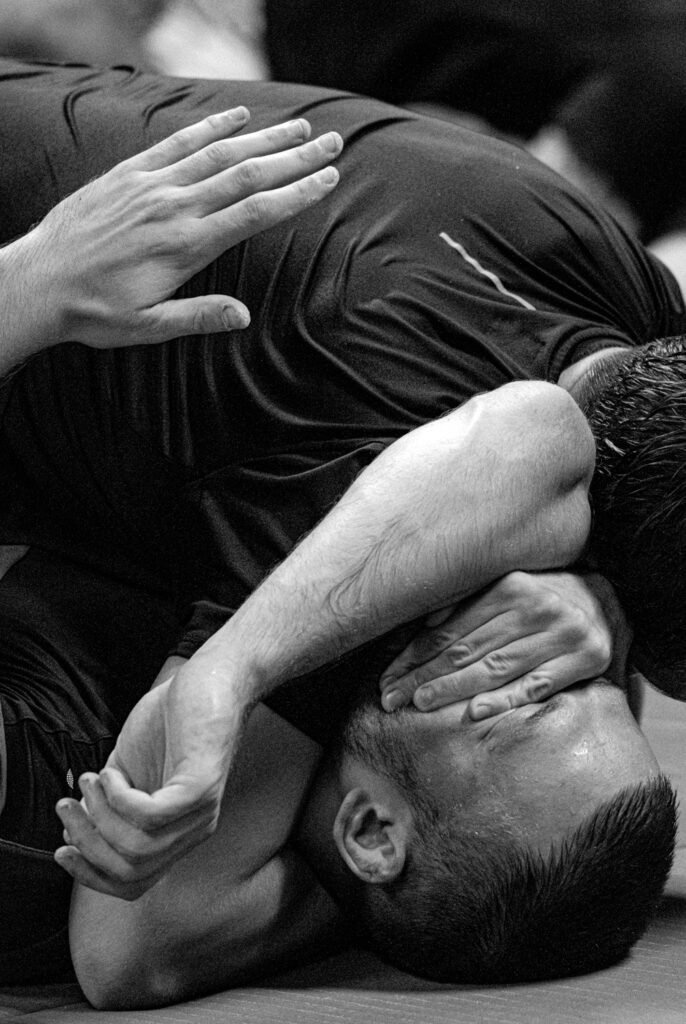Die Aufnahme zeigt einen Mann, der eine Brazilian Jiu-Jitsu Übung im Studio von Spike’s Gym in Berlin-Köpenick ausführt. Im Hintergrund sind weitere Personen zu sehen, die ebenfalls an der Übung teilnehmen.