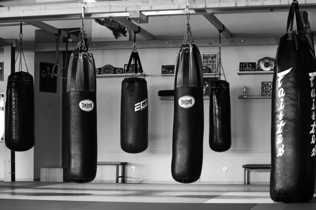 Die Aufnahme zeigt einen Innenraum eines Kampfsportstudios, das sich auf Kampfsportarten wie Thaiboxen spezialisiert hat. Im Vordergrund befinden sich mehrere Boxsäckke an der Decke. Es handelt sich um das Ringside Gym in Lichtenberg, Berlin.
